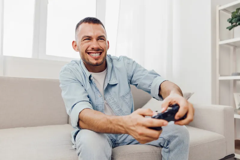 A smiling man enjoying gaming at home, embracing solo living and mental well-being. The scene reflects a blend of leisure and emotional minimalism in a cozy space.