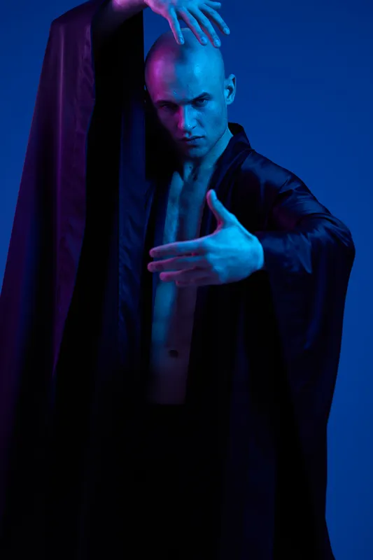 Striking man in dramatic pose, wearing a flowing black garment, exuding strong emotions. The lighting enhances a mystique atmosphere and highlights his physique.