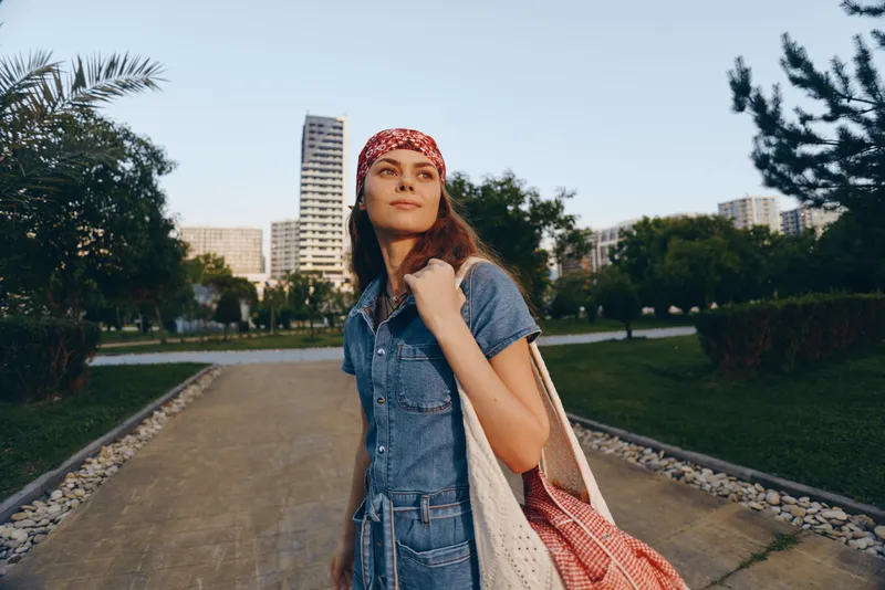 Lifestyle woman in modern boho-western denim street style walking confidently outdoors with a red bandana, natural light, and film color effect.