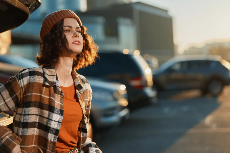 Woman portrait with beanie and sunlight in parking lot, candid lifestyle moment with authenticity and golden hour glow, mindful living vibe and emotional storytelling in urban scene