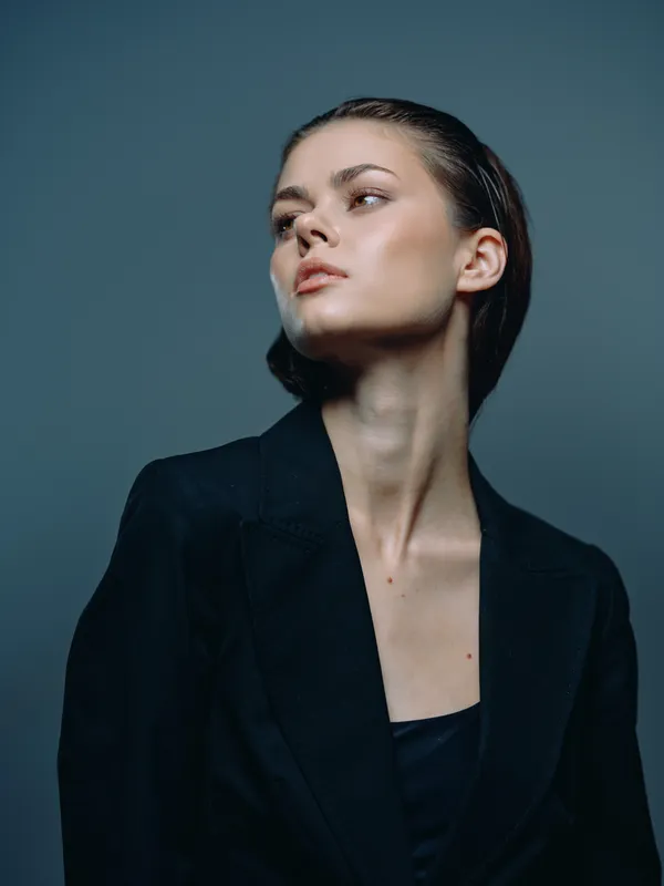 Elegant woman in dark blazer looking away with a confident and thoughtful expression on a gray background.