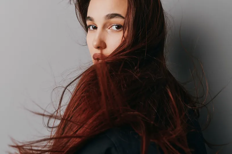 Young woman with long flowing hair looking over shoulder against plain background, natural makeup and soft lighting for beauty portrait and fashion concept.