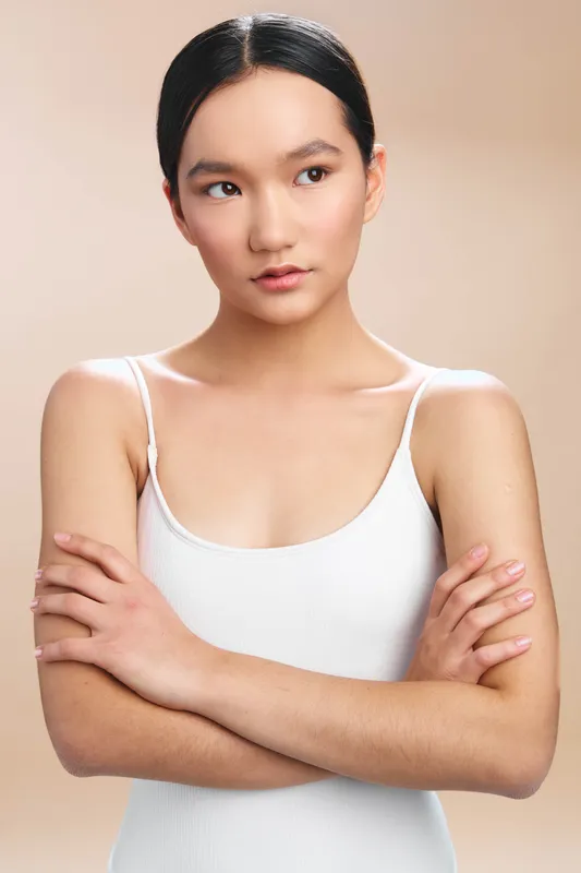 Asian woman stands in a studio setting with arms crossed and a composed expression, presenting a calm and confident portrait suitable for marketing, fashion, or corporate use.
