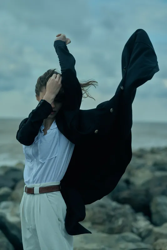 Wind swept cape and dress on a dynamic beach scene, showcasing dramatic movement, outdoor fashion, and bold motion in a coastal landscape