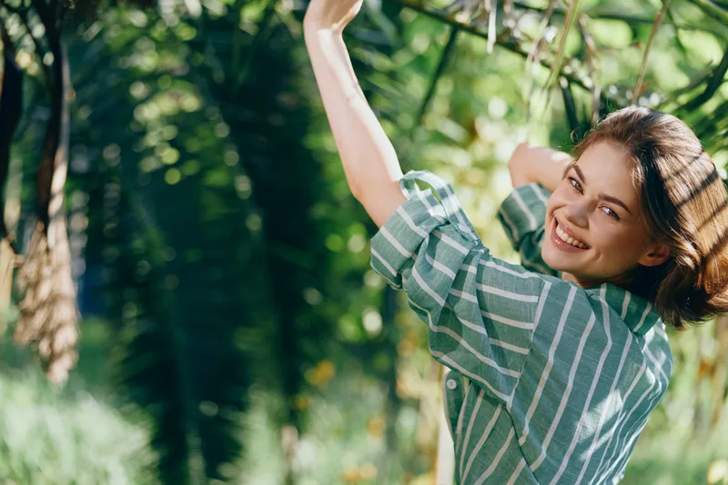 woman, outdoors, nature, smiling, cheerful woman stands among trees with sunlight, embodying happiness, confidence, and freedom in a serene, fresh outdoor moment