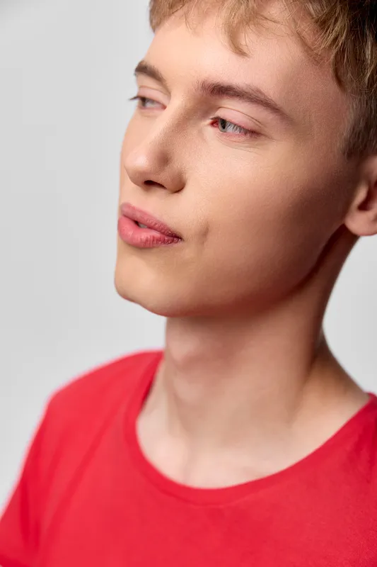 Young man, thoughtful profile, closeup of face in a red shirt, calm gaze and soft lighting, minimal background, expressive mood, studio vibe and natural skin tone emphasis