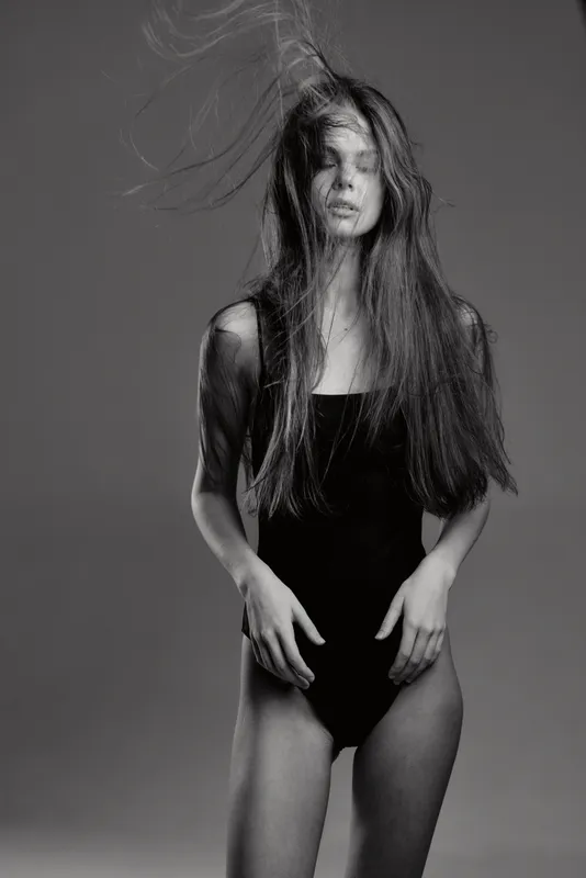 Black and white portrait of a woman with long hair in a dark outfit expressing emotion and movement.