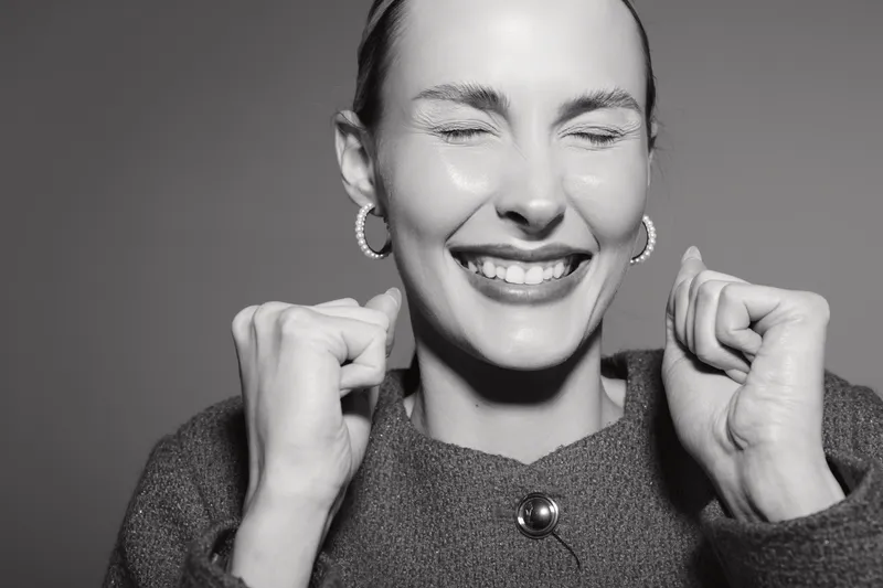 Happy white woman with fair skin and closed eyes smiles with clenched fists in studio. Concept of joy, success, and positive emotion.