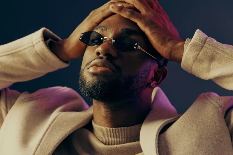 Thoughtful man in trendy attire with sunglasses, conveying emotions of contemplation against a soft gradient background