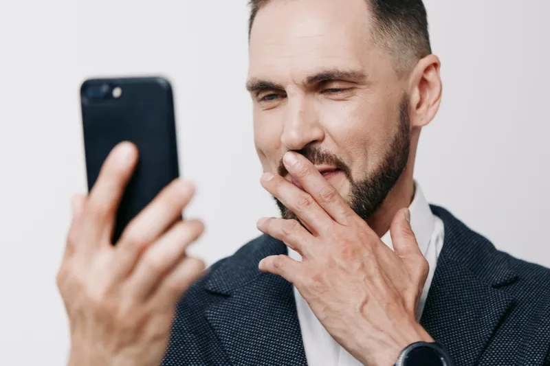A professional man in a dark blazer checks his smartphone, depicting a focused business moment. He pauses with a thoughtful gesture, set against an isolated colored background.