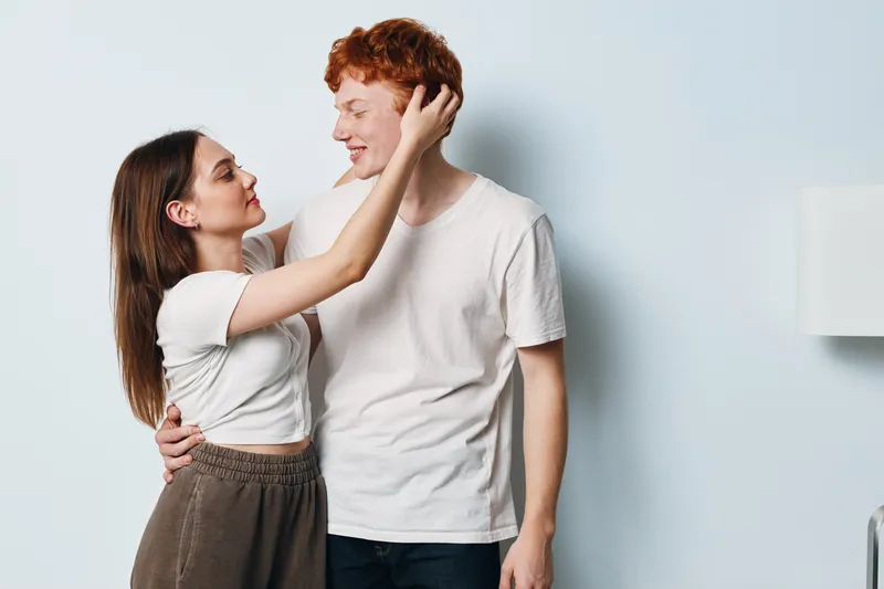 Couple, young man and woman embracing and looking at each other with affection indoors. Romantic relationship, casual clothing and light background with gentle emotion and connection.