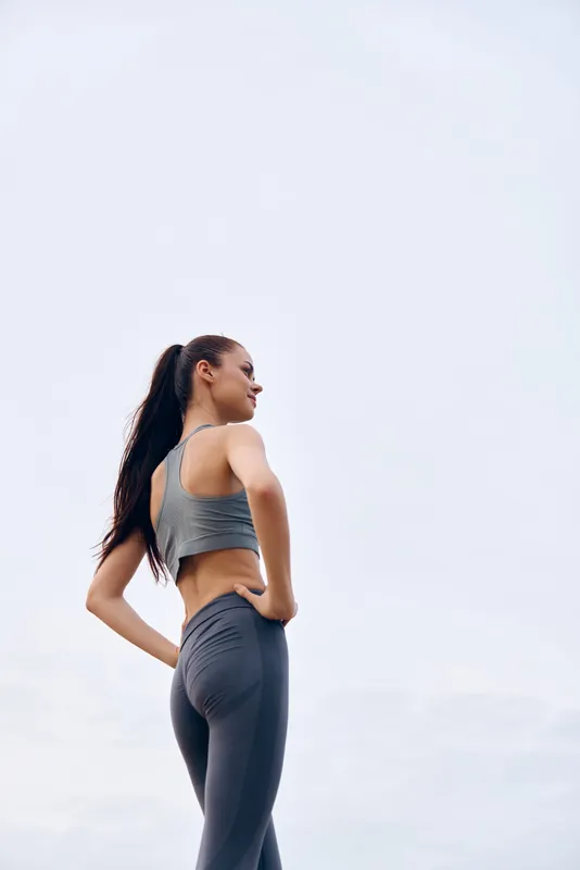 Young athletic woman in gray sportswear posing confidently against a minimalist background, conveying strength and determination in fitness