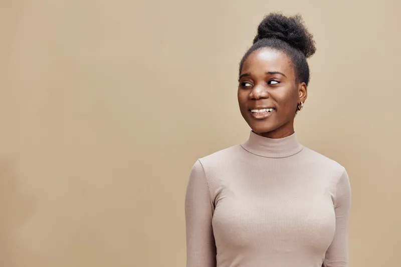 Smiling Black woman in a beige turtleneck, exuding confidence and warmth against a soft brown background, perfect for wellness and fashion concepts