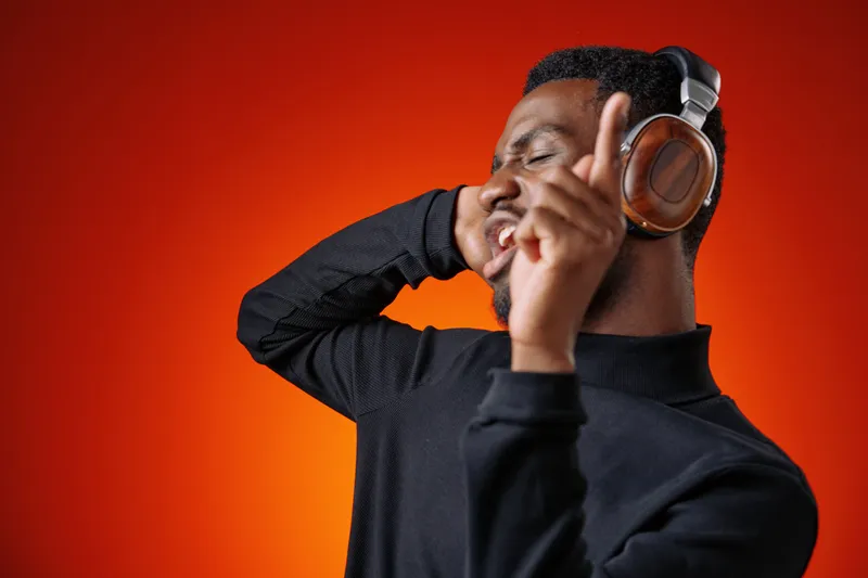 Happy young man enjoying music with headphones in a vibrant orange background, showcasing joy and emotion in a modern style