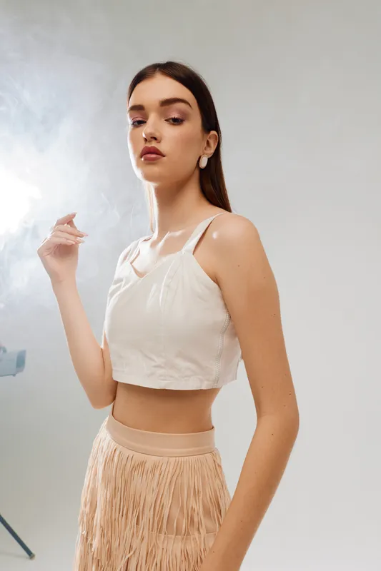 Young woman beauty fashion model poses in stylish beige top and fringed skirt. Studio portrait with soft lighting on neutral background. Concept for fashion and elegance.