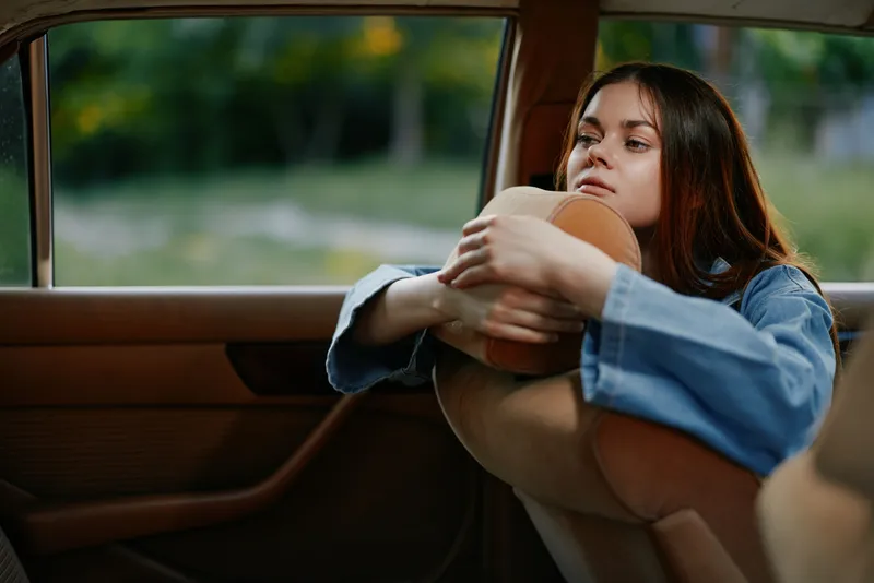 Thoughtful young woman gazing out the car window, dressed in casual denim, reflecting emotions while embracing a cozy interior, evokes a sense of nostalgia.