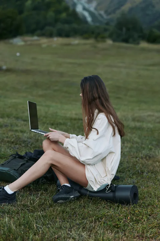 A focused individual sits on grass with a laptop outdoors, enjoying a tranquil work moment in nature while exploring ideas and staying productive away from the desk.