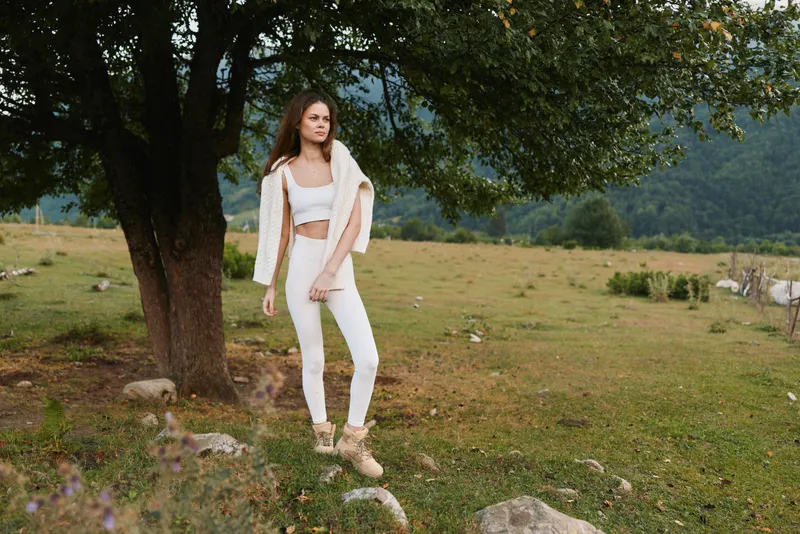Casual woman outdoors wearing a white outfit in a meadow with trees, showcasing a relaxed lifestyle, natural beauty, and carefree fashion under soft daylight and mood today.