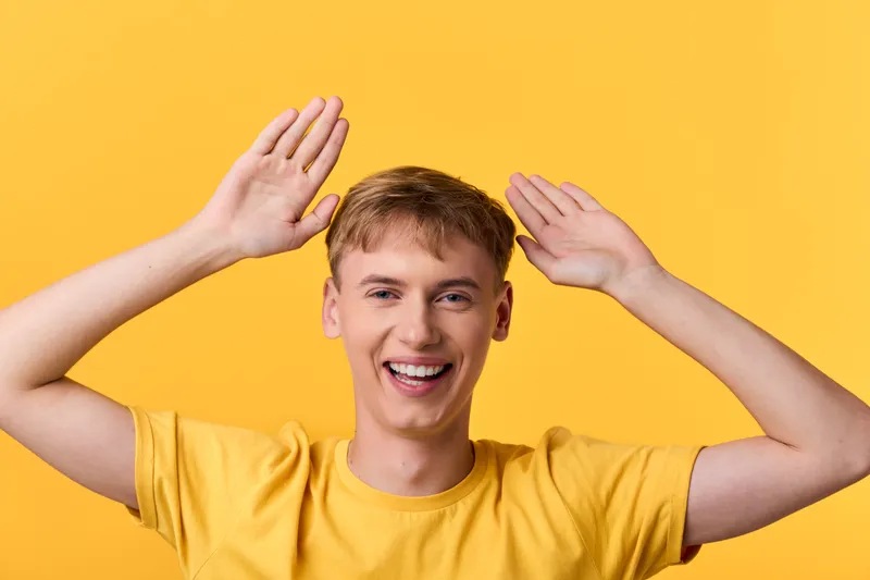 Smile, man with yellow background, raised hands, cheerful energy for an upbeat lifestyle, positive vibe, and friendly branding in promotional media