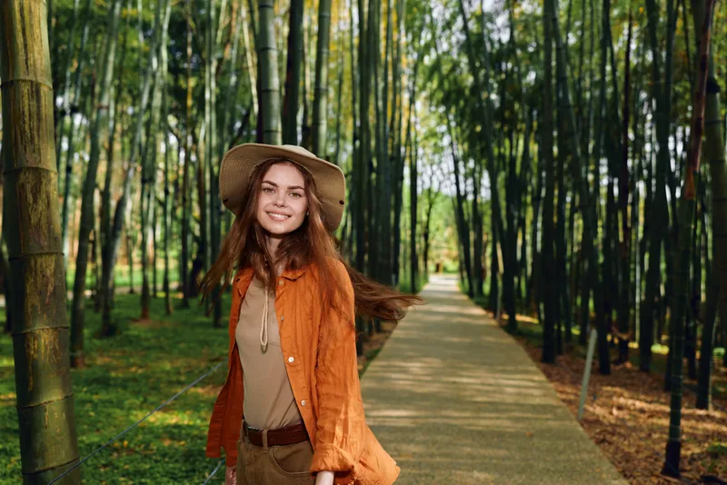 Woman smile hat bamboo path forest nature outdoors walking travel lifestyle fashion casual jacket straw happy young portrait model in a serene sunlit grove, peaceful outdoor portrait and leisure