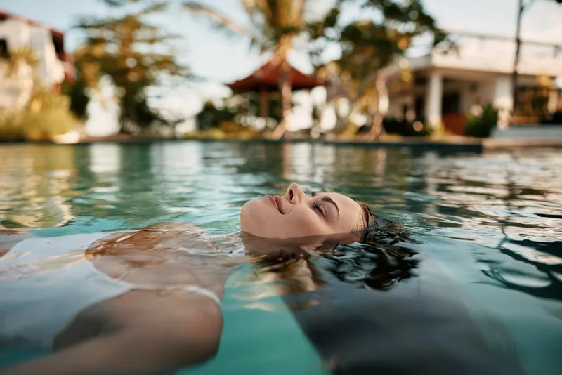 Relaxed person floating in a sunlit pool, enjoying outdoor leisure and tranquil water, warm surroundings and gentle breeze create a carefree vacation mood