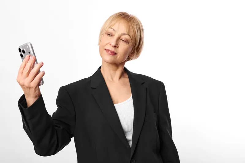 Woman holding smartphone, senior professional in business blazer, smiling in a portrait on a white background, calm communication concept about technology and confidence, hand on phone