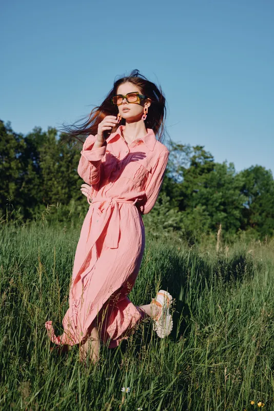 Beautiful young model in a pink dress enjoying the summer outdoors, showcasing vibrant fashion in nature with a joyful expression, perfect for lifestyle images