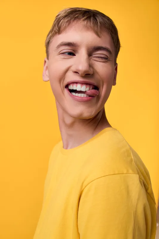 Smile, winking, yellow, background, cheerful, young, man, shirt, casual, fashion, closeup portrait style with bright teeth and playful mood, sunny yellow backdrop highlighting friendly energy