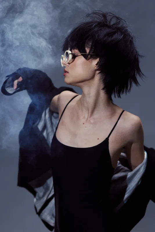 Stylish woman with short hair wearing sunglasses and a black dress in a smoky atmosphere