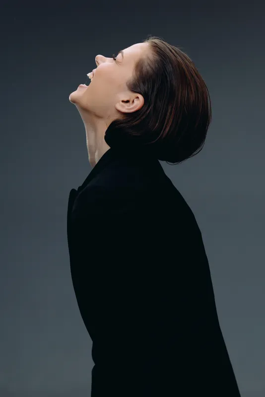 Smiling woman with short hair laughing joyfully in black outfit, isolated on dark background, expressing happiness and freedom.
