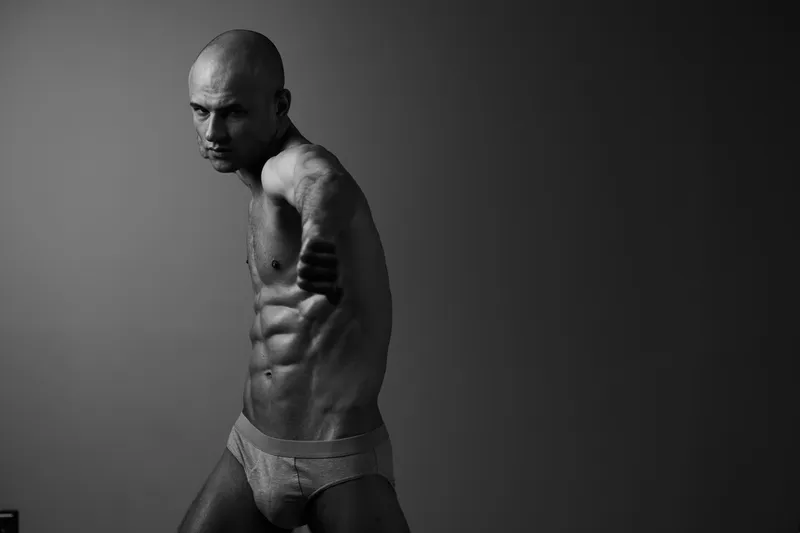 Dynamic black and white image of a man showcasing strength and confidence, with a focus on muscular physique and determined expression.