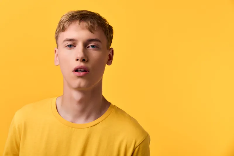 Young man with a surprised expression against a bold yellow background, wearing a casual yellow shirt in a studio setting, highlighting mood, color harmony, and fashion.