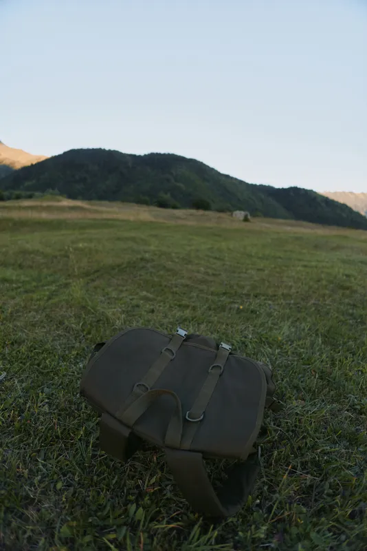 Brown leather bag lying on green grass in open field with hills and clear sky in background natural outdoor scene peaceful environment