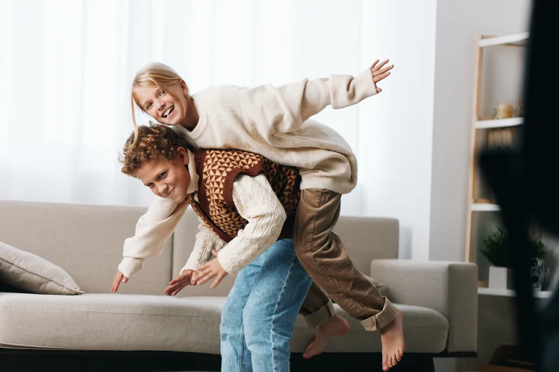 Authentic moment of play as kids laugh and race on a living room couch, capturing a spontaneous lifestyle scene rooted in school memories and family warmth.