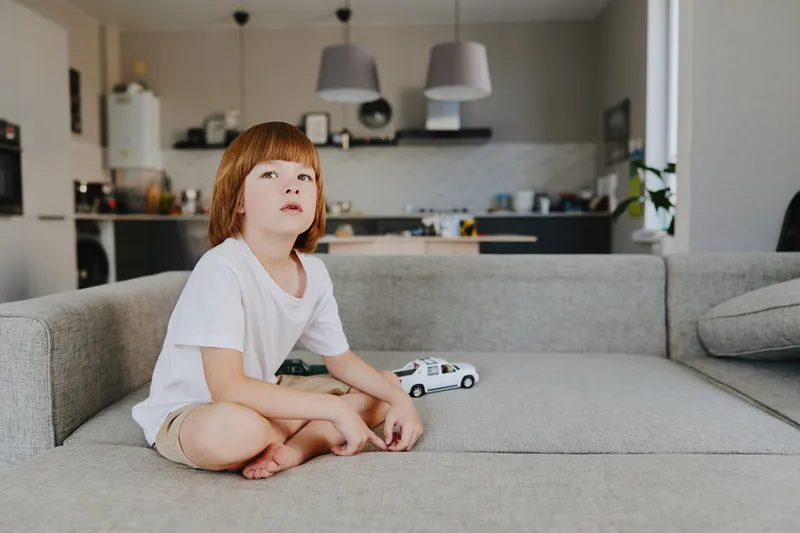 Thoughtful boy sitting on a sofa, playing with a toy car in a cozy living room. A peaceful moment capturing childhood imagination and creativity.