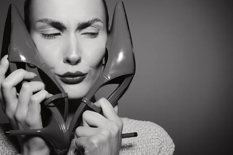 Caucasian woman with light skin holding red high heels near face in black and white image, expressing emotion.