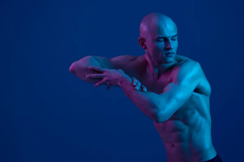 Man posing gracefully against a blue background, showcasing athletic build and expressive movement. The image emphasizes dynamic shapes and vibrant lighting.
