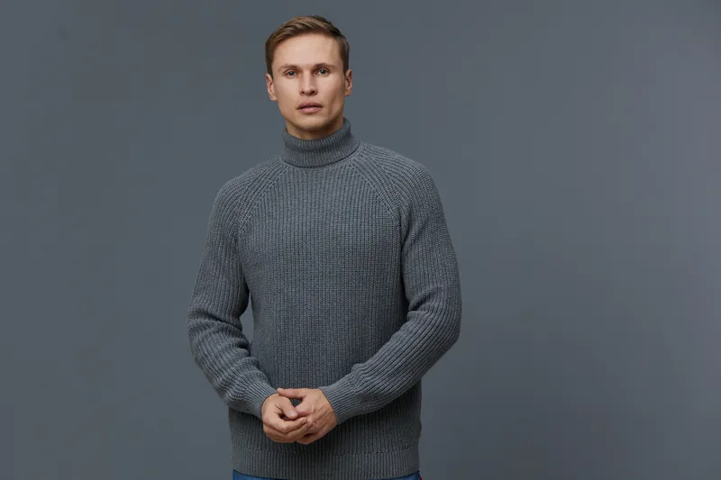 Young caucasian man wearing grey knitted sweater standing isolated on dark grey background looking at camera digital nomad concept
