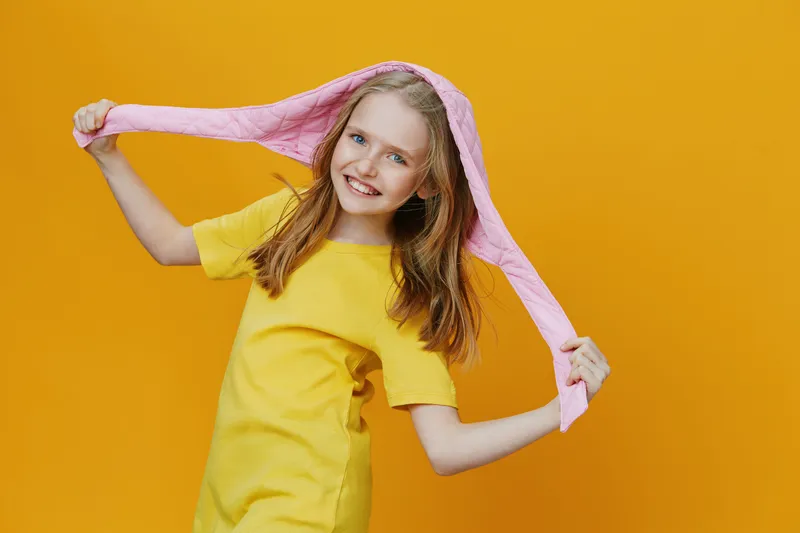 Youthful girl in a yellow dress with a pink hoodie, smiling happily against a bright yellow background Perfect for cheerful and youthful themes