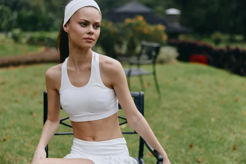 Young female fitness model in white activewear, posing gracefully in a serene outdoor park setting, reflecting a healthy lifestyle and mindfulness