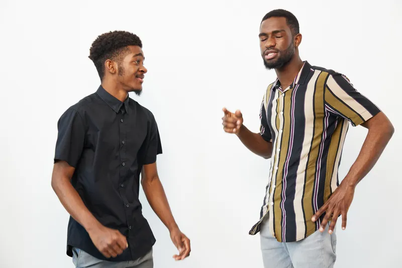 Two smiling Black men having a joyful conversation, dressed casually, showcasing camaraderie and friendship in a bright, minimalistic setting.