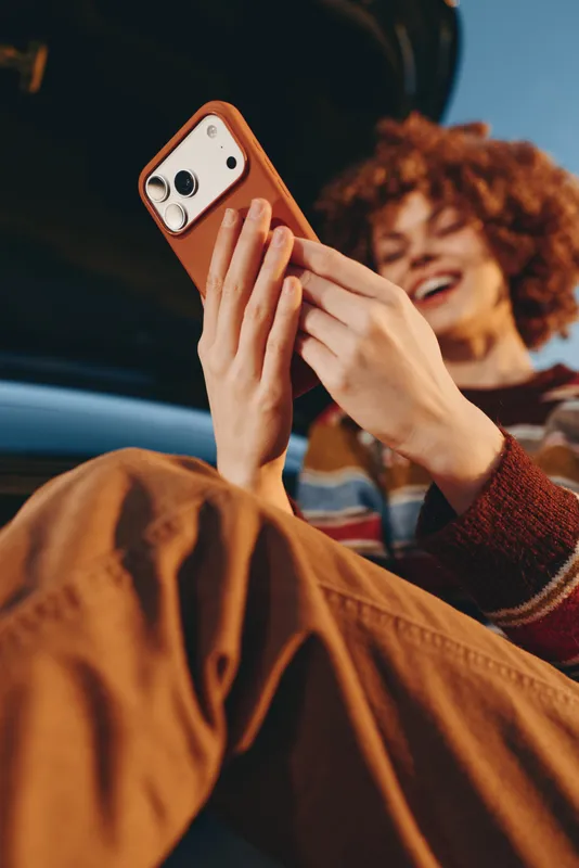 Woman lifestyle in car, smartphone in hands up front, communication with lit screen, curly hair woman smiling in background, casual travel technology moment, warm cozy light
