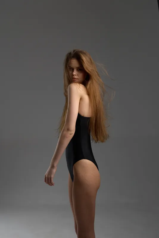 slender woman in black swimsuit posing in studio with grey background, elegant fashion, long hair, minimalist style