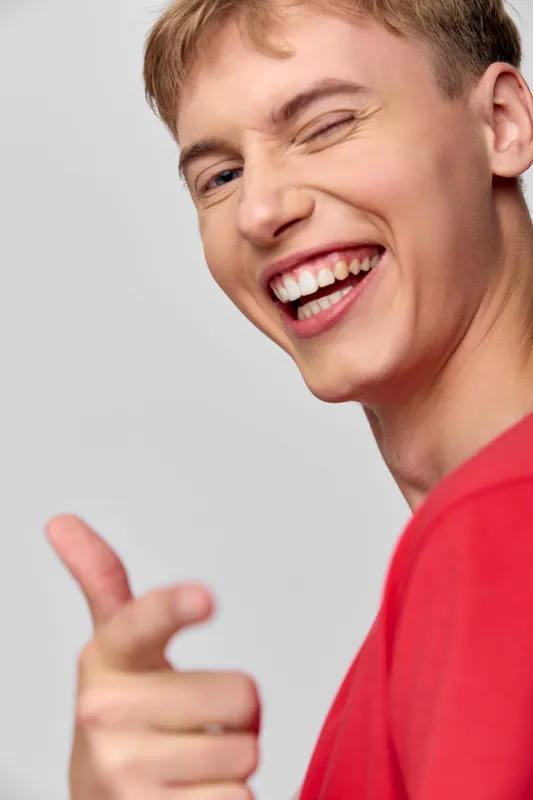 Close up of smiling figure giving a thumbs up and winking, wearing a red shirt, bright studio lighting, positive mood, friendly and energetic expression for marketing