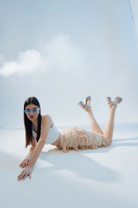 Young woman in fashionable summer outfit poses on the floor under soft natural light. Concept of beauty, fashion, and modern style with a minimalistic background.