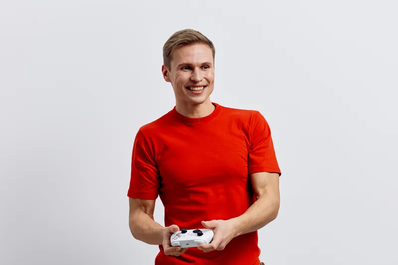 Smiling man in red t-shirt holding game controller isolated on plain white background. People lifestyle concept, casual, joyful, entertainment, leisure, male, young adult, positive energy, relaxed, fu