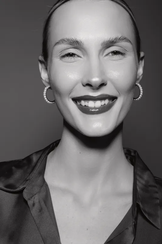 Smiling white woman with light skin and earrings looks happy in a black and white close up portrait photo.