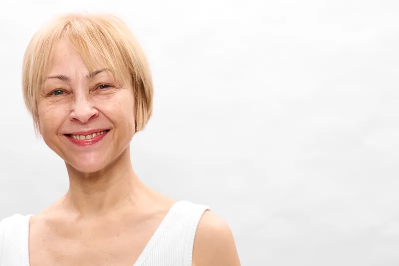 Woman portrait, smiling senior, blonde hair, elderly woman, studio lighting, white background, gentle expression, relaxed posture, soft skin, close up
