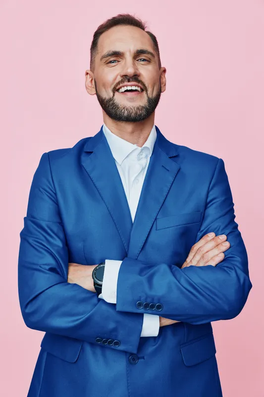 Professional man in a blue suit stands against a solid pink background, projecting confidence and focus while radiating calm, determination, and optimistic energy.
