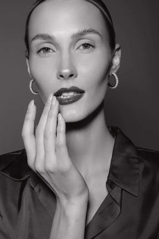 Close-up portrait of a pale white woman with light skin and slicked back hair touching her face in a studio. Concept of beauty, skincare, and elegance.